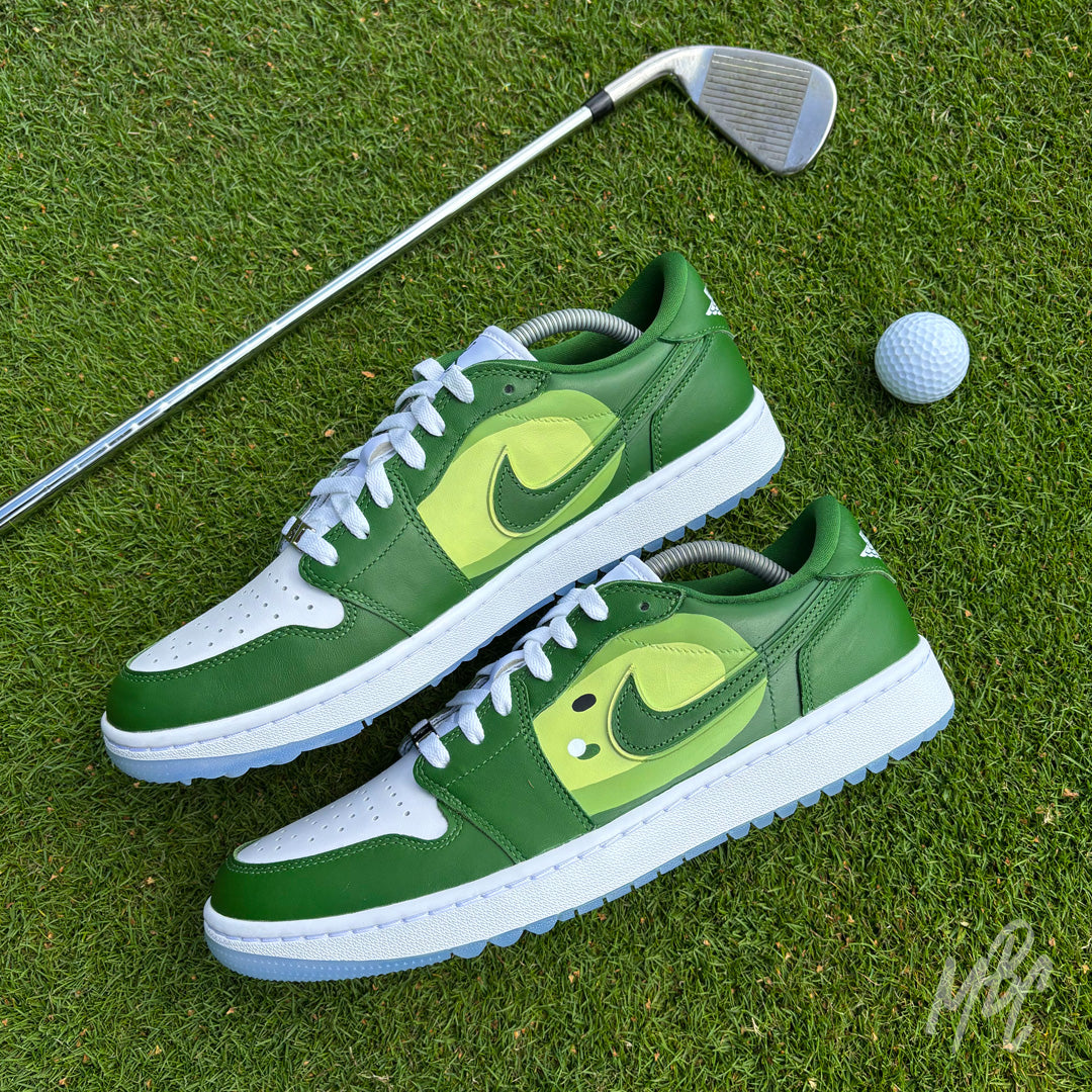 Pair of Pin Position custom Jordan 1 Low Golf shoes with hand-painted golf fairway artwork displayed on a putting green beside a golf club and ball.
