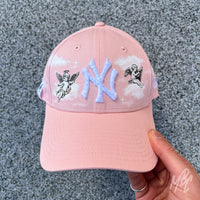 Pink New Era NY custom cap with angel cherub graphics and hand painted cloud design shown in lifestyle shot