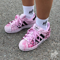 Pair of Pink Overgrown custom Adidas Superstar trainers worn on foot with hand-painted flowers, textured pink finish and Overgrown branding.