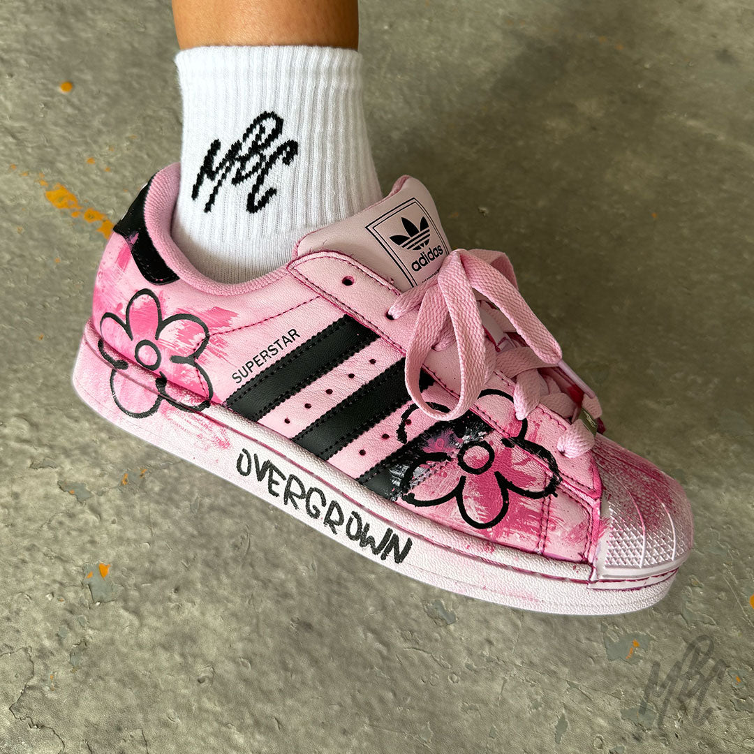 Close-up of the Pink Overgrown custom Adidas Superstar on foot, showcasing hand-painted pink flowers, textured brushstroke effects, black Adidas stripes and custom "Overgrown" midsole artwork.