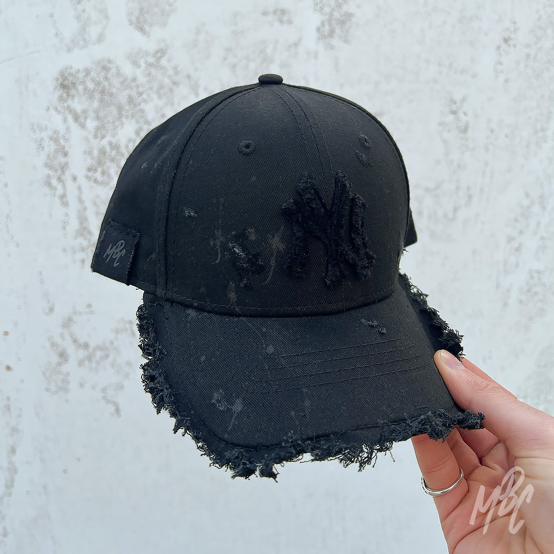 Raw Edge New Era NY custom cap in black with distressed brim and frayed NY logo held outdoors