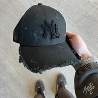 Black Raw Edge New Era NY custom cap with distressed details and frayed peak worn in hand lifestyle shot
