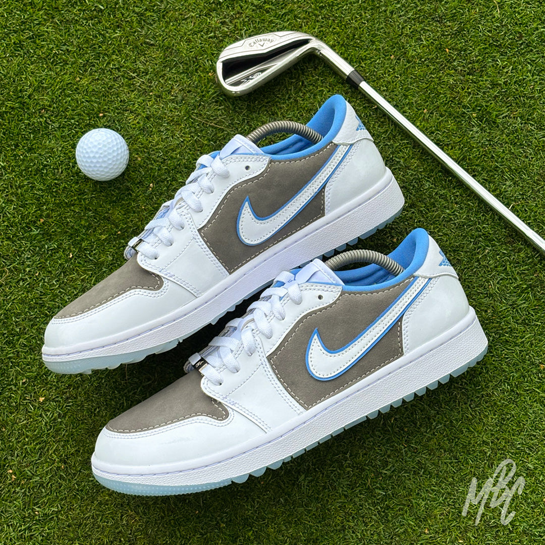 Slate Suede custom Jordan 1 Low Golf shoes featuring grey suede panels, white leather and light blue accents, photographed on a golf green with a golf club and ball.