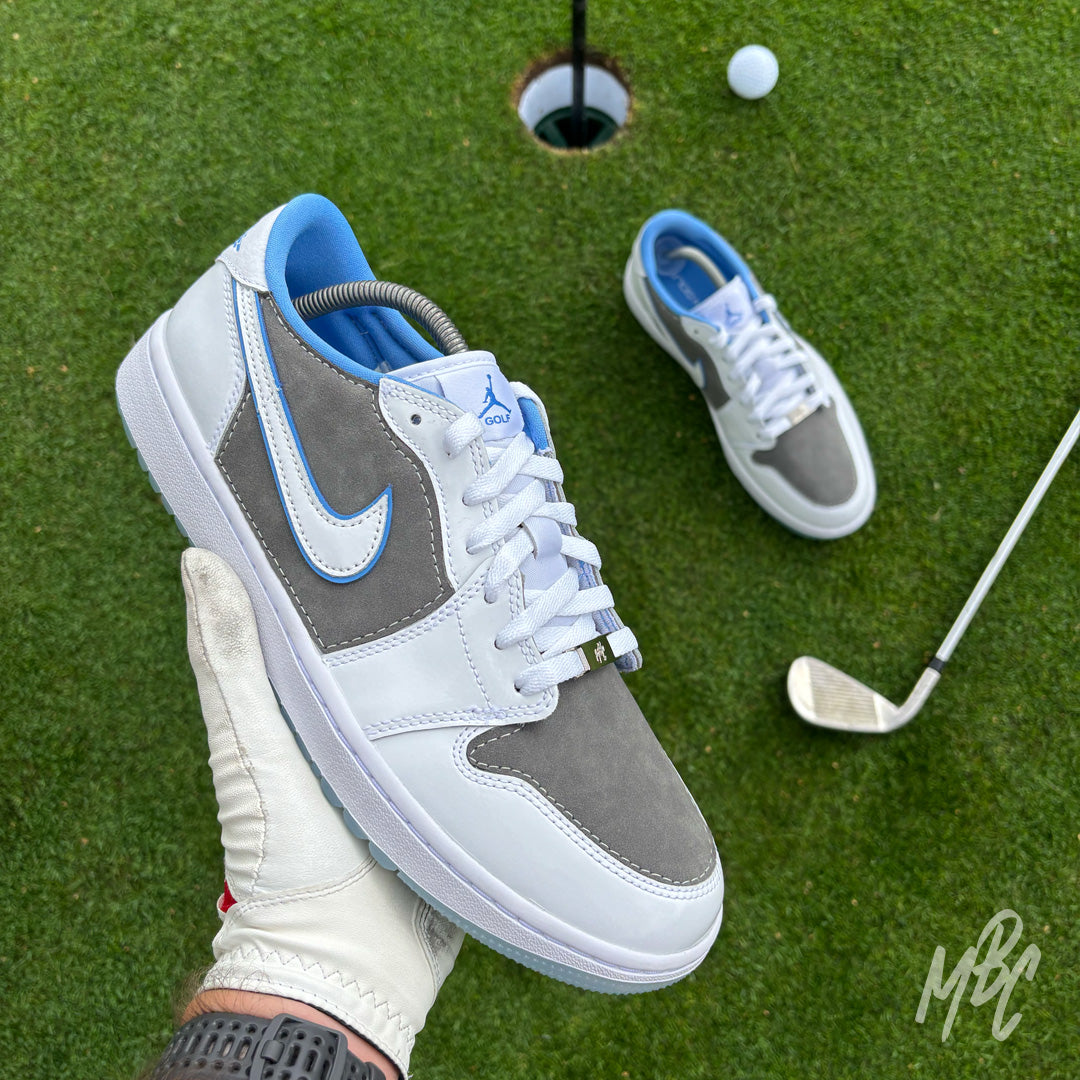 Slate Suede custom Jordan 1 Low Golf shoes held above a putting green, featuring premium grey suede, white leather and light blue detailing.