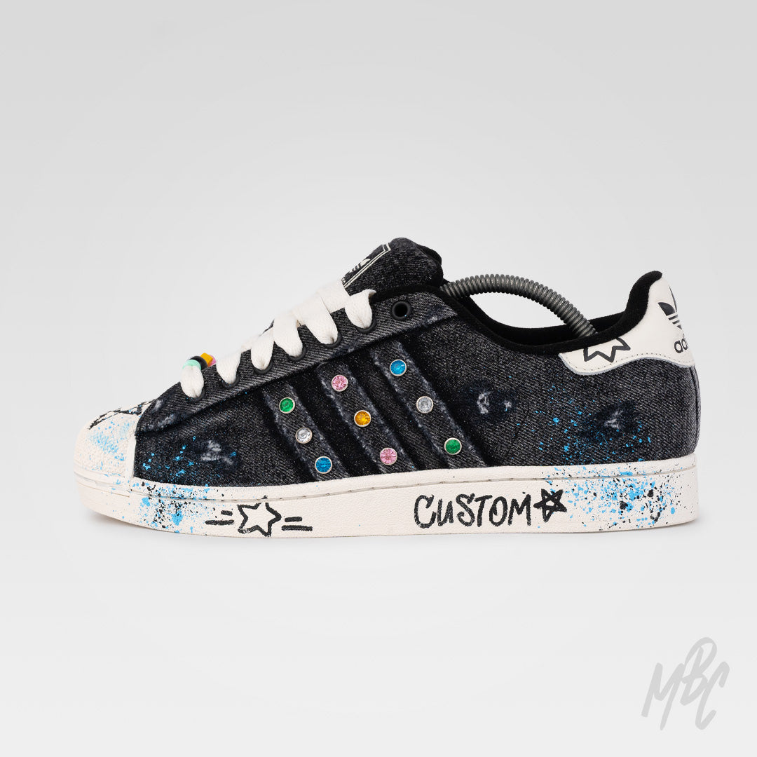 Outside view of Stardust Denim custom Adidas Superstar with distressed black denim, colourful gem embellishments, blue paint splatters and hand-painted graphics.