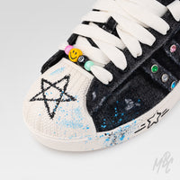 Close-up of Stardust Denim custom Adidas Superstar with distressed black denim, hand-painted star artwork, blue paint splatters and colourful lace bead charms.