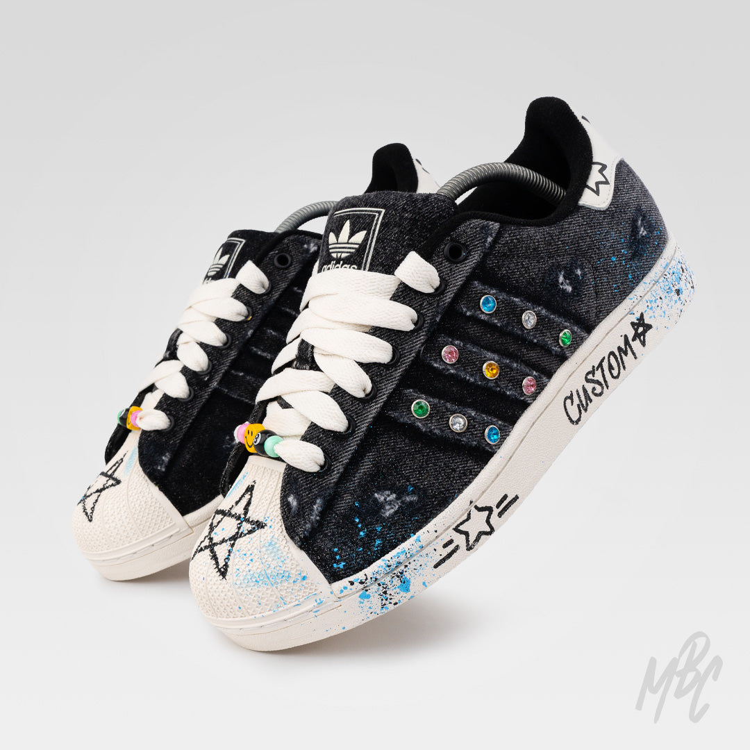 Pair of Stardust Denim custom Adidas Superstar trainers featuring distressed black denim, hand-painted stars, colourful gem detailing, paint splatters and custom lace beads.