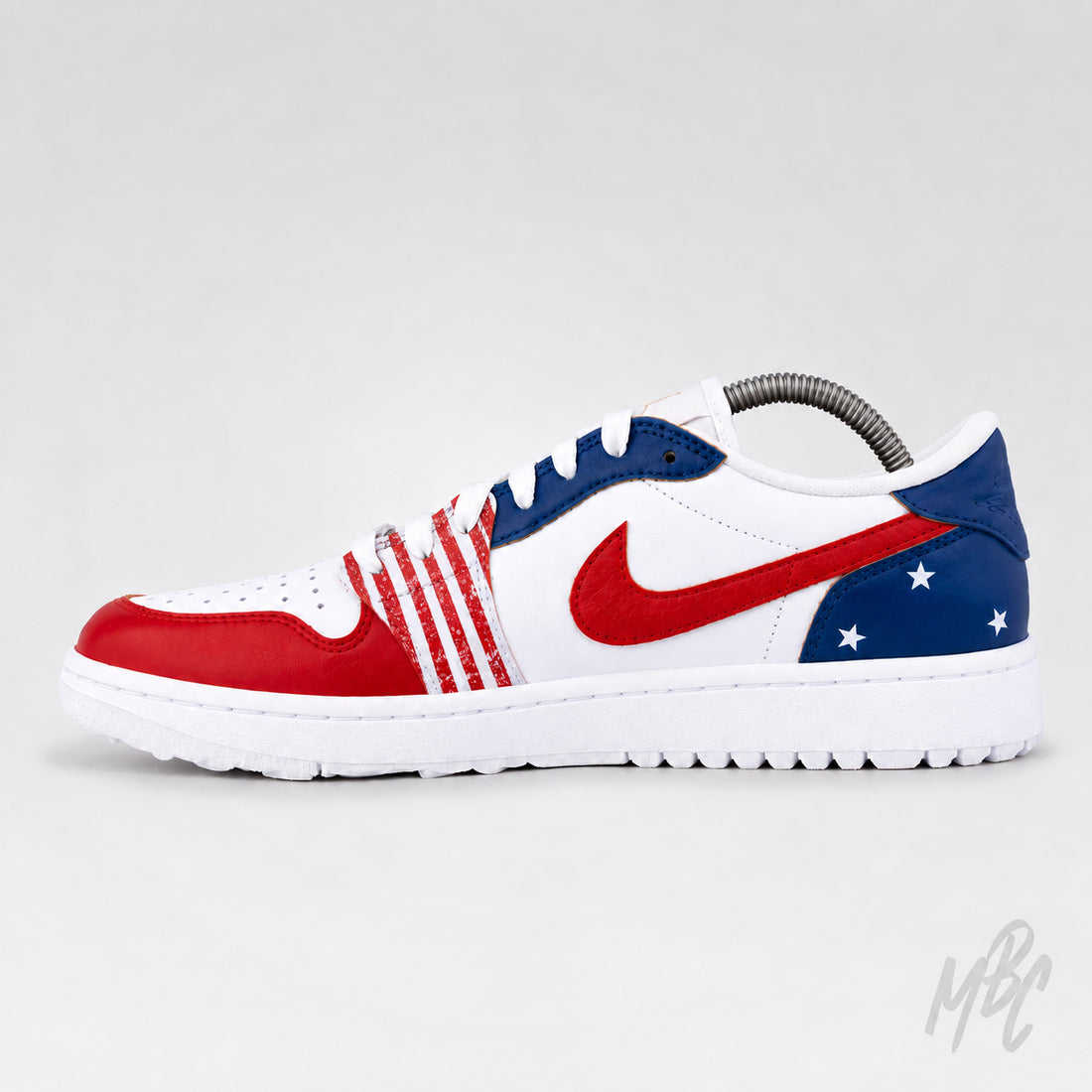 A Nike Jordan 1 Low sneaker featuring a patriotic red, white, and blue color scheme. The white leather base is accented with a red toe cap, red stripes on the side, a red Swoosh, and a blue heel section decorated with white stars.
