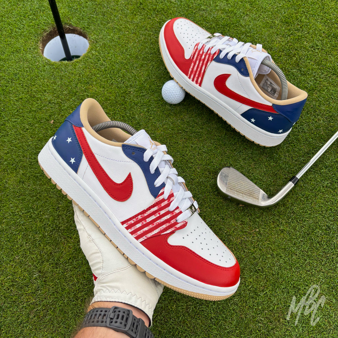 Stateside Drive custom Jordan 1 Low Golf shoes held above a putting green, featuring hand-painted patriotic red, white and blue with a golf club and golf ball.