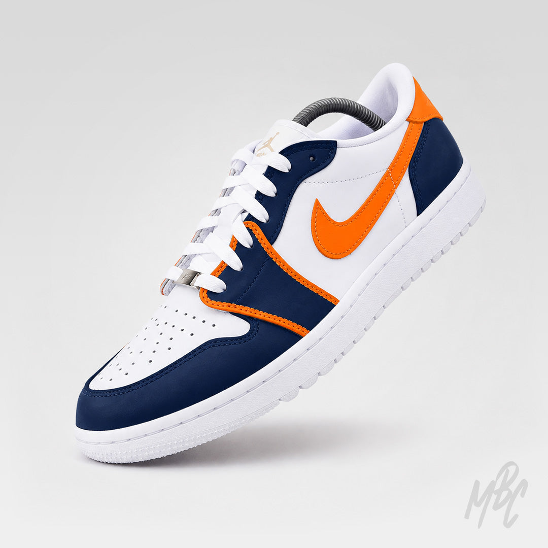 Angled front view of a white Air Jordan 1 Low Golf shoe with navy overlays, bright orange trim and Nike Swoosh, white laces, and a perforated toe box.
