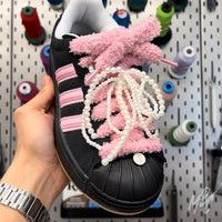 Black Adidas Superstar trainers with thick pink fluffy shoelaces, pearl lace charms and custom sneaker accessories