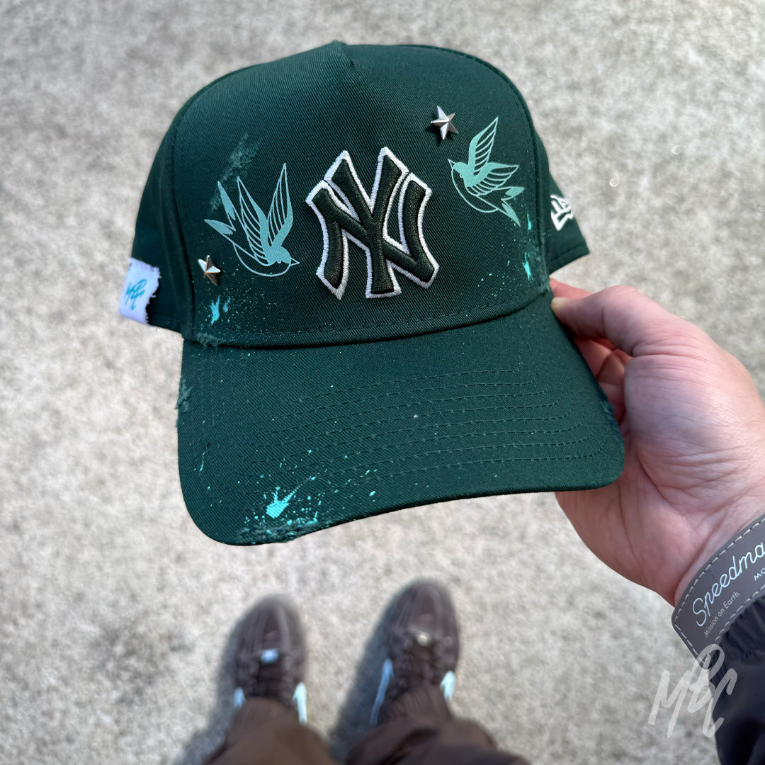 Green Twin Swallow New Era NY custom cap with bird illustrations and paint splatter shown in hand lifestyle shot