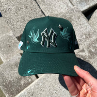 Twin Swallow New Era NY custom cap in green with swallow graphics, star studs and paint splatter detail held outdoors