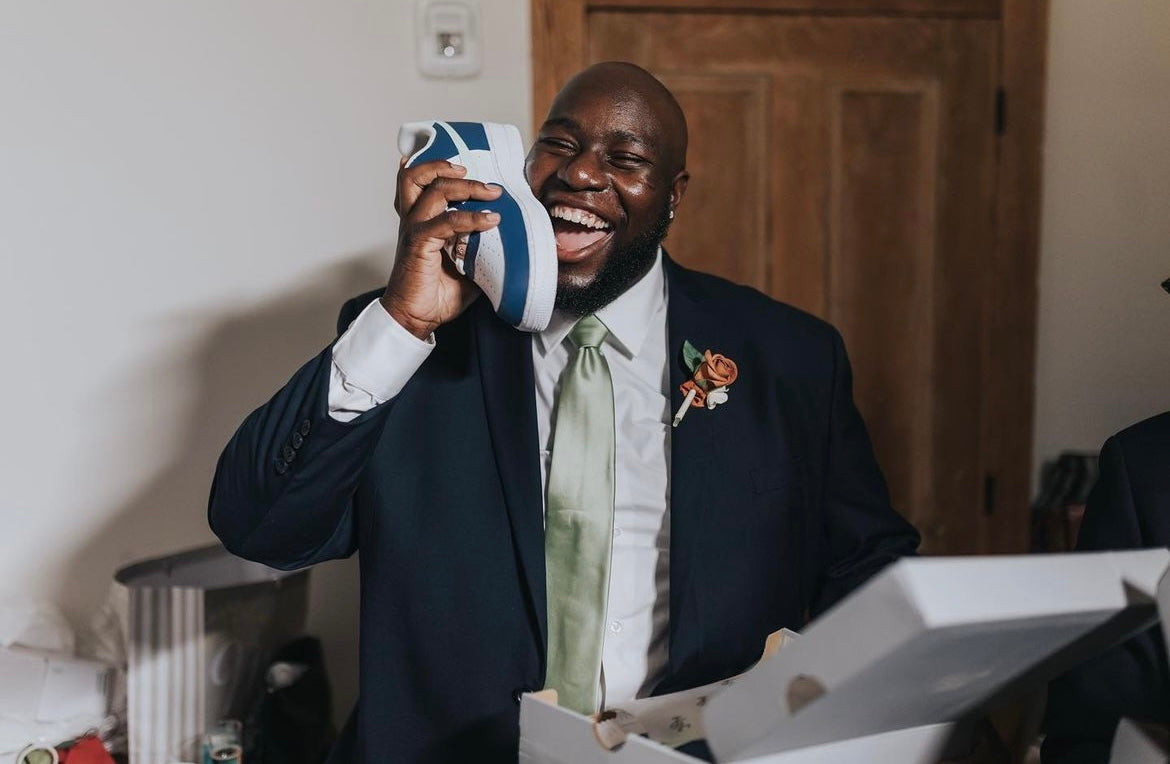 Groom's man laughing holding up a custom Jordan 1 low sneaker at a wedding