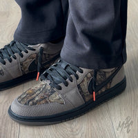 Woodland Camo Jordan 1 Low worn on foot with black laces and camo toe box detail