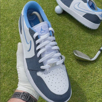 Close-up video showcasing custom navy suede and white golf shoes on a golf course, including detailed shots of the suede panels being stitched, silver lace locks, blue accents and the finished shoe held up against the fairway.