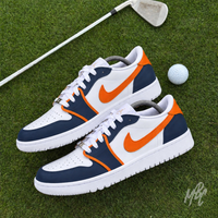 Two custom navy, white and orange golf shoes positioned on a putting green beside a golf ball and silver golf club.